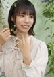 A woman in a white blouse holding a plant in her hand.