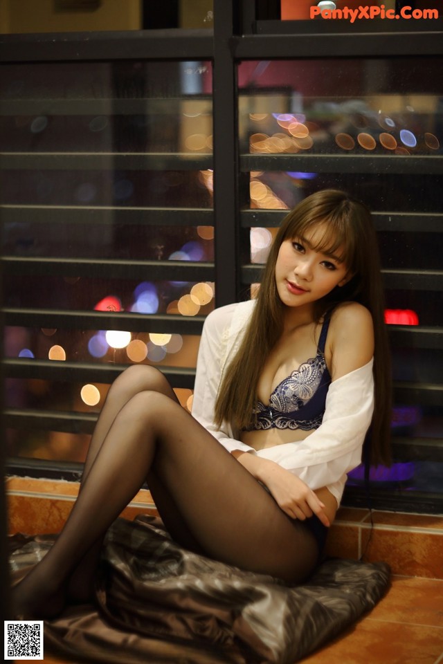 A woman sitting on a bed in front of a window.