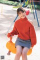 A woman in an orange sweater sitting on a yellow ball.