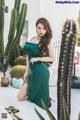 A woman in a green dress posing in front of a cactus.