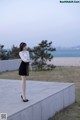 A woman in a white blouse and black skirt standing on a concrete wall.