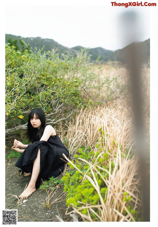 A woman in a black dress sitting on the ground.